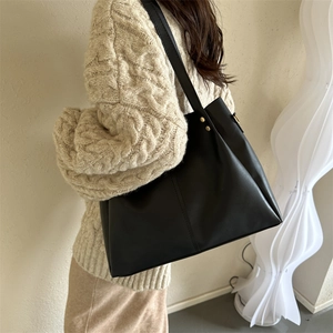 Minimalist black PU leather tote bag with gold metal accents worn over a beige knit sweater