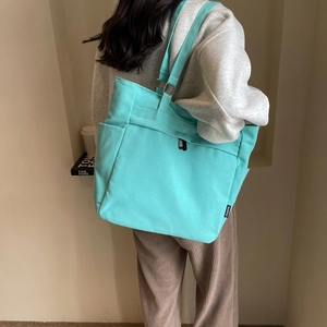 Detail view of mint green canvas tote bag with side pocket and fashion woven label on strap