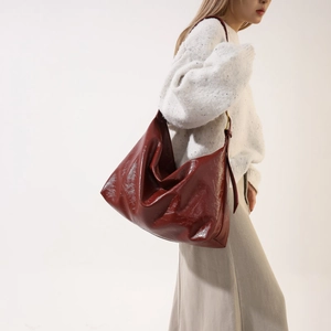 Side view of large burgundy patent leather hobo bag with natural folds on a model
