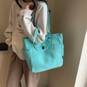 Detail of mint green canvas tote bag showing fashion label and dual strap design