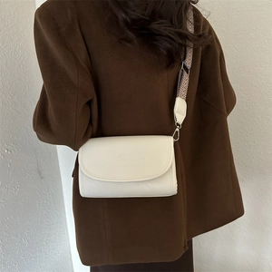 Detail of white leather crossbody bag with geometric striped fabric strap and flap closure