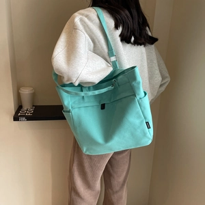 Detail of mint green canvas tote bag with side pocket and fashion woven label on strap
