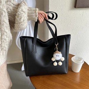 Minimalist black PU tote bag detail with white plush cartoon monster pendant on a table
