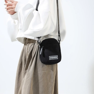 Detail of black corduroy crossbody bag with FASHION label and adjustable strap