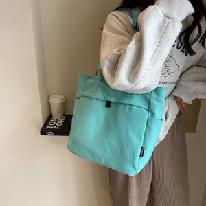 Close-up of mint green canvas tote bag featuring a black FASHION tag and side pockets