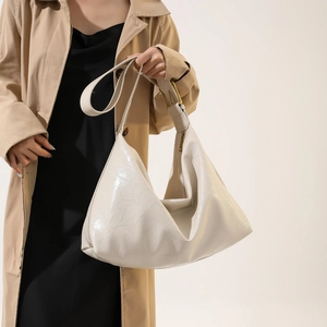 Detail of a creamy white oversized hobo bag with glossy finish and wide shoulder strap