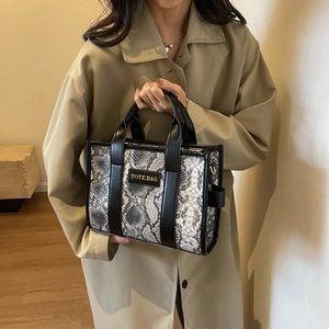Detailed view of snake skin pattern tote bag held by a model in khaki trench coat