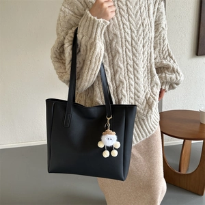 Detail of minimalist black PU leather tote bag featuring a cute white plush pendant