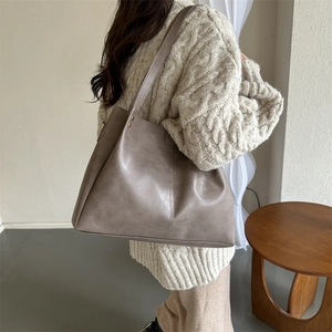 Detail view of large brown PU leather tote bag with gold rivets worn on model shoulder