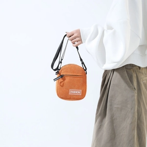 Detail of an orange corduroy crossbody phone bag with fashion label and nylon strap
