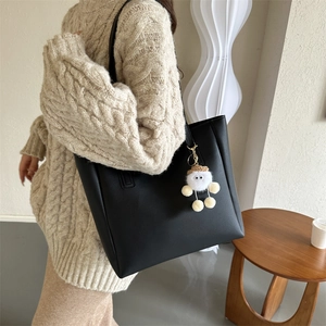 Lifestyle shot of black minimalist PU leather tote bag with a white plush doll charm
