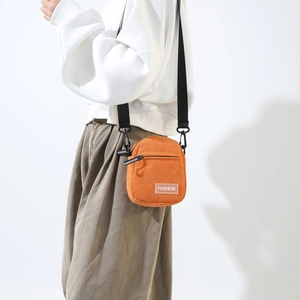 Detail of orange corduroy crossbody bag with adjustable nylon strap and fashion label