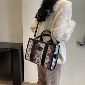 Fashionable snake print tote bag with black leather straps worn by a model in a modern room