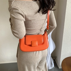 Detailed view of an orange PU leather crossbody bag worn by a model in a beige sweater