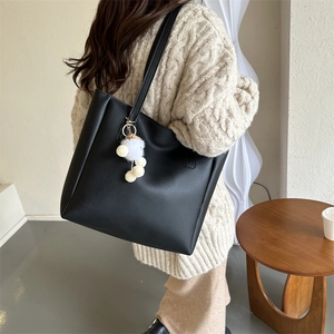Detail of black PU tote bag with a white plush pompom charm shown on a model