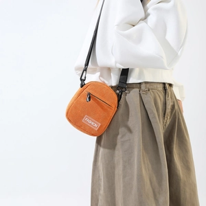 Close-up of orange corduroy bag featuring a FASHION patch and adjustable black nylon strap