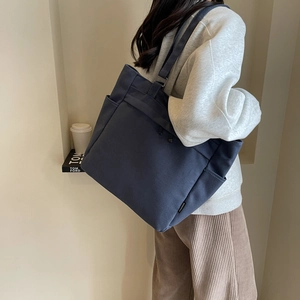 Detail of dark blue canvas tote bag side pockets and wide strap on a model