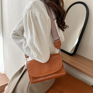 Brown PU crossbody bag with wide geometric pattern strap shown in a lifestyle setting
