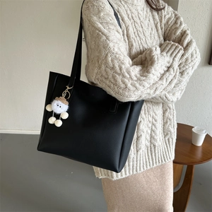 Detail view of black PU tote bag with soft plush charm accessory and long shoulder straps