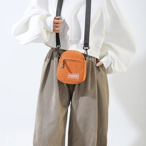 Close-up of orange corduroy crossbody bag with fashion label and adjustable strap