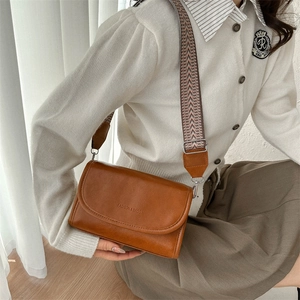 Close-up of brown PU leather crossbody bag with wide woven strap and fashion lettering