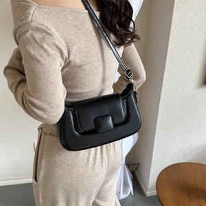 Detail of minimalist black PU leather underarm bag with gold metal buckle and matte finish
