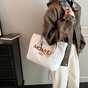 Detail of white faux fur tote bag with embroidered branding and brown leather shoulder strap