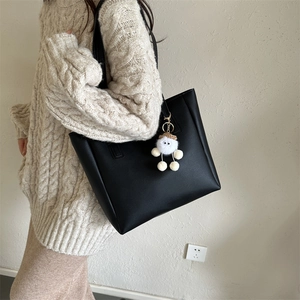 Detail of minimalist black PU leather tote bag featuring a cute white plush doll charm