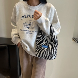 Detail of plush zebra print handbag with blue logo tag held by model in casual wear