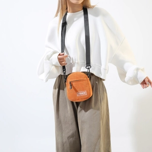 Detail of an orange corduroy crossbody bag with adjustable black nylon shoulder strap