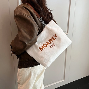 Detail of white faux fur tote bag featuring embroidered logo and leather chain strap