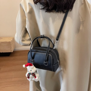 Detail of black crossbody bag with white stitching and cute plush bear accessory