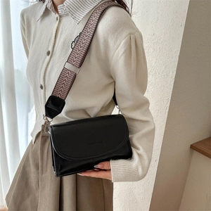 Detail of black PU leather crossbody bag featuring fashion text and wide woven shoulder strap