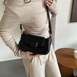 Detail of minimalist black PU leather shoulder bag with gold hardware and square buckle