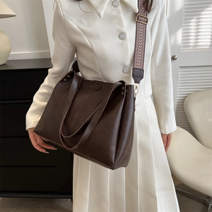 Dark brown matte leather tote bag with wide geometric strap shown on a female model