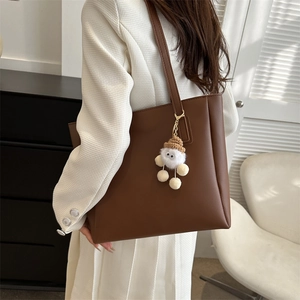 Dark brown PU leather tote bag with monster charm shown on a white luxury outfit