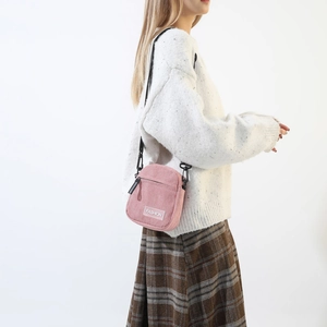 Detail of pink corduroy crossbody bag featuring a front zipper pocket and fashion label