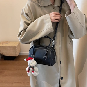 Detail of black Boston bag with white stitching and plush bear charm on beige coat