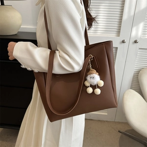 Detail view of deep brown tote bag with cute plush charm on minimalist white outfit