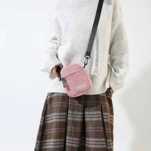 Close-up of pink corduroy crossbody bag with fashion label and black nylon strap
