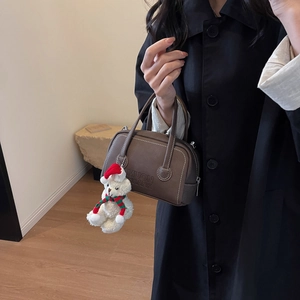Detail of dark brown leather crossbody bag with brand engraving and festive plush bear charm
