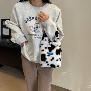 Close-up of plush handbag with cow print pattern and blue label held by a model