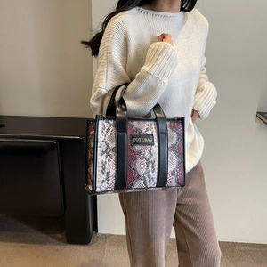Detail of pink and grey snakeskin tote bag with black handles and text patch