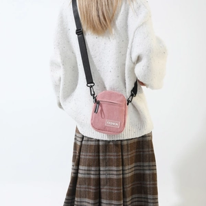 Detailed texture of pink corduroy crossbody bag with fashion label and nylon strap