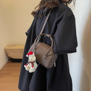 Detailed side view of a brown leather Boston bag with white stitching and bear charm