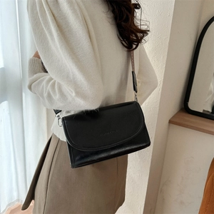 Detail of a black half-moon PU crossbody bag featuring a textured woven shoulder strap