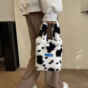 Close-up of cow print plush handbag featuring a signature blue woven brand label