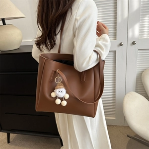 Detail of minimalist dark brown PU leather tote bag with white plush charm on white dress