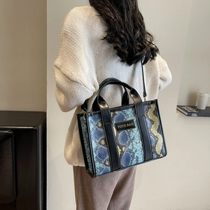 Detail of blue and yellow python texture tote bag shown on a white knitted sweater
