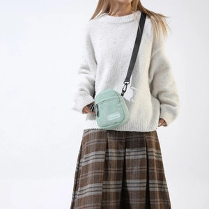 Close-up of light green corduroy crossbody bag with adjustable strap and fashion label